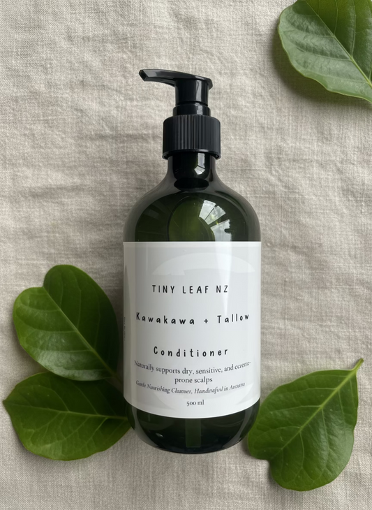 Dark green bottle of Kawakawa tallow conditioner on linen surface with Kawakawa leaves Tiny Leaf NZ