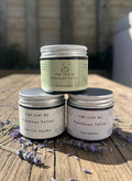 Three small containers of Tiny Leaf NZ tallow on a wooden surface with a blurred background.