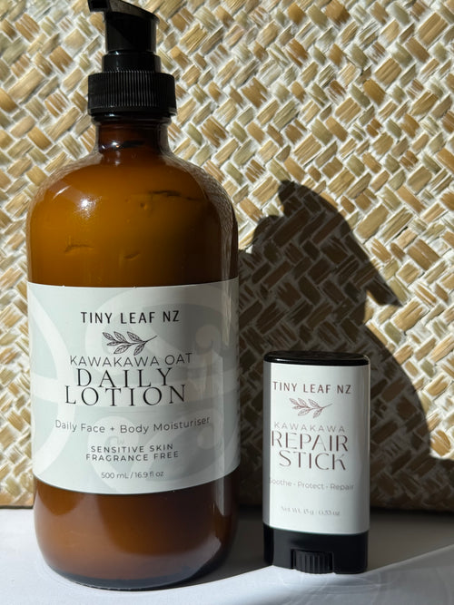 A 500 mL amber bottle of Tiny Leaf NZ Kawakawa Oat Daily Lotion stands next to a matching 60 g stick of Tiny Leaf NZ Kawakawa Repair Stick against a woven basket background.