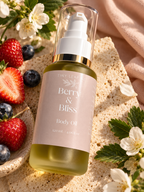 A bottle of Tiny Leaf Berry & Bliss Body Oil, filled with golden-yellow oil and featuring a pale pink label, styled on a textured beige surface with fresh strawberries, blueberries, white blossoms, and soft pink fabric.