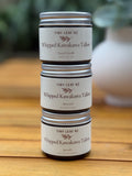 Stack of Tiny Leaf NZ whipped kawakawa tallow products on a wooden surface with a blurred natural background.