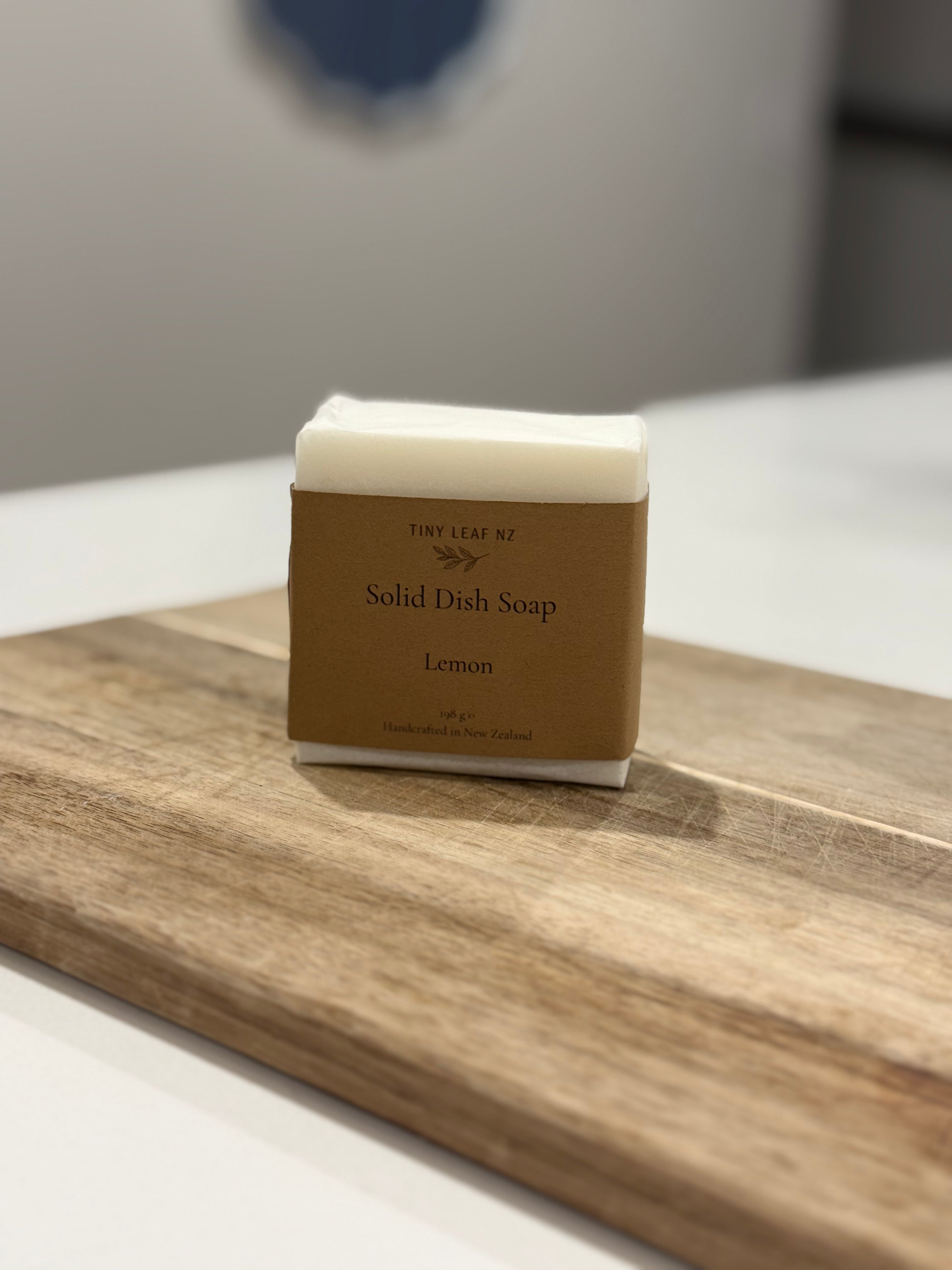 A bar of Tiny Leaf N.Y. Solid Dish Soap, Lemon scent, resting on a wooden cutting board on a white countertop.