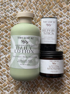 Three Tiny Leaf NZ natural skincare products arranged on a woven straw mat: a large pale green bottle of Kawakawa Oat Daily Lotion, a white tube of Kawakawa Repair Stick, and a dark amber jar of Yellow Kawakawa Unscented.