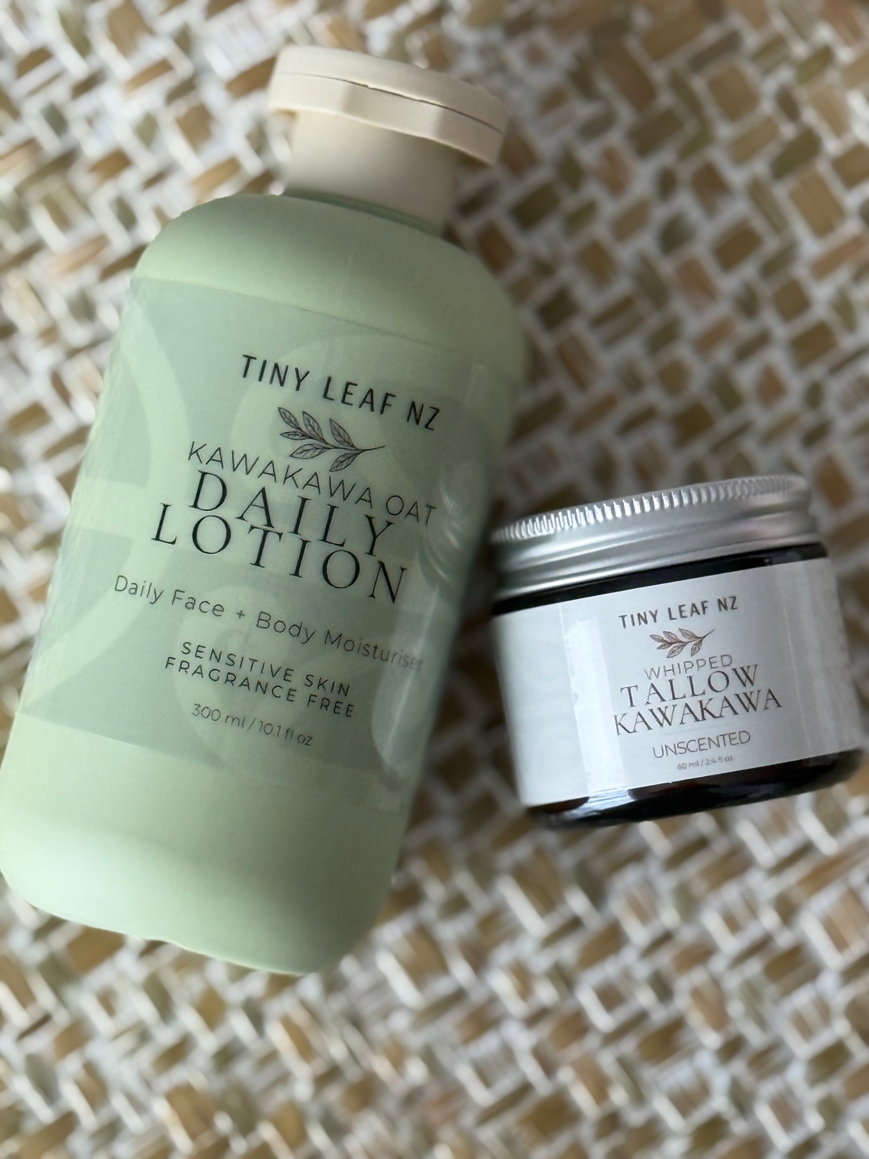 Tiny Leaf NZ Kawakawa Oat Daily Lotion in a pale green pump bottle next to a small jar of Tallow Kawakawa Unscentled, displayed on a woven straw mat.