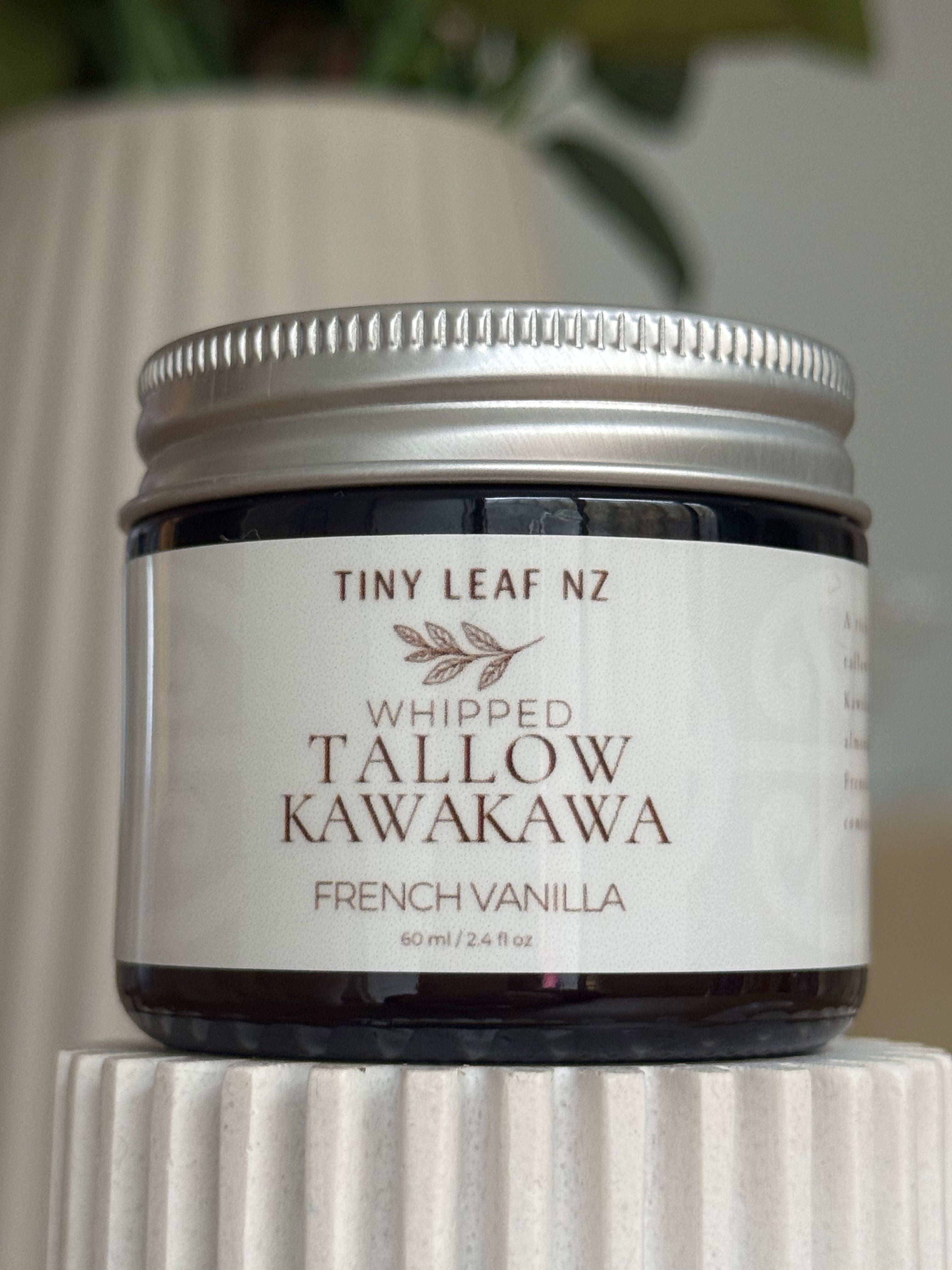 A jar of Tiny Leaf NZ Whipped Tallow Kawakawa French Vanilla balm, featuring a white label and silver metal lid, displayed on a white ribbed pedestal.