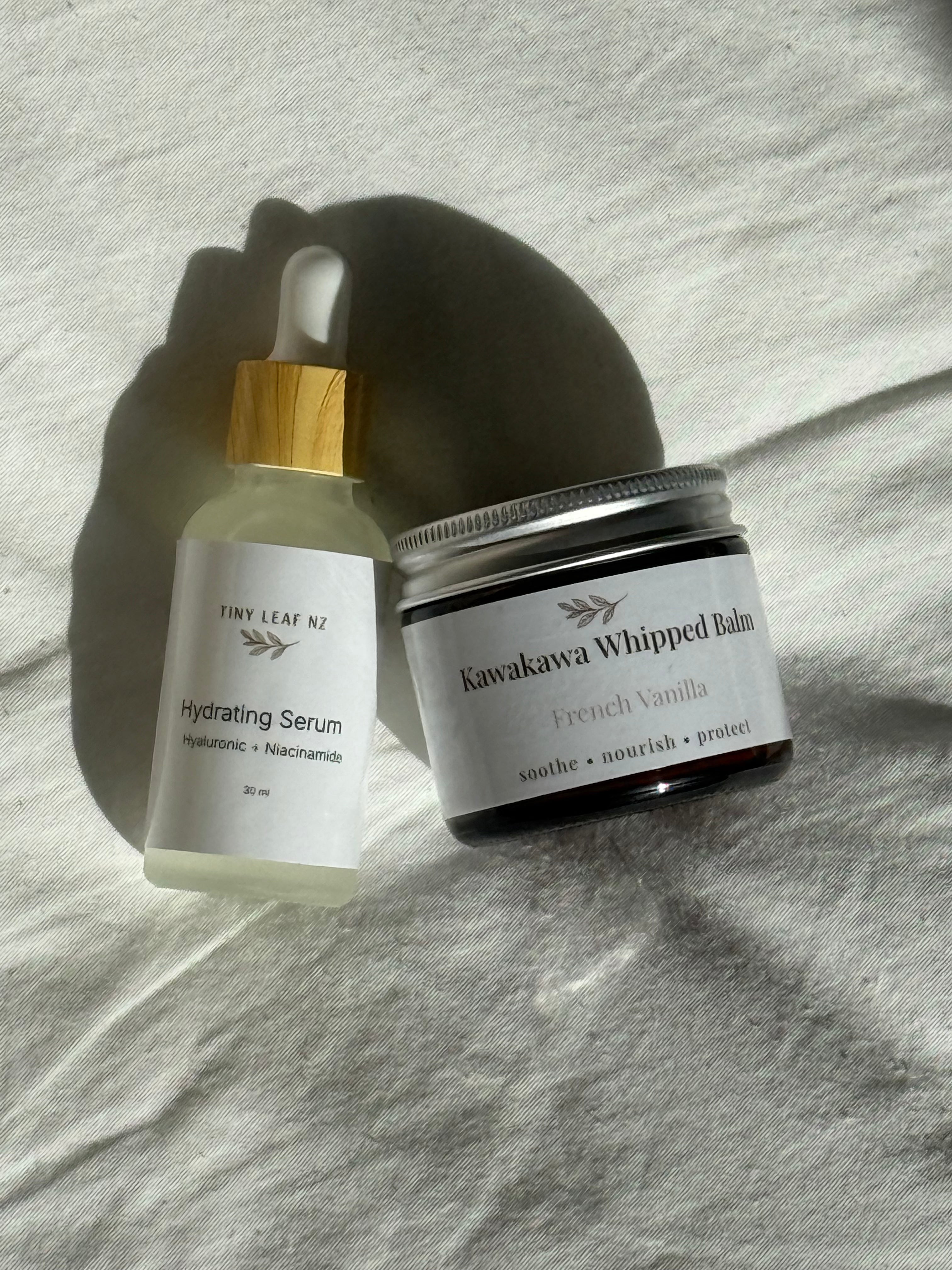 Hydrating Serum and Kawakawa Whipped Balm on a textured surface