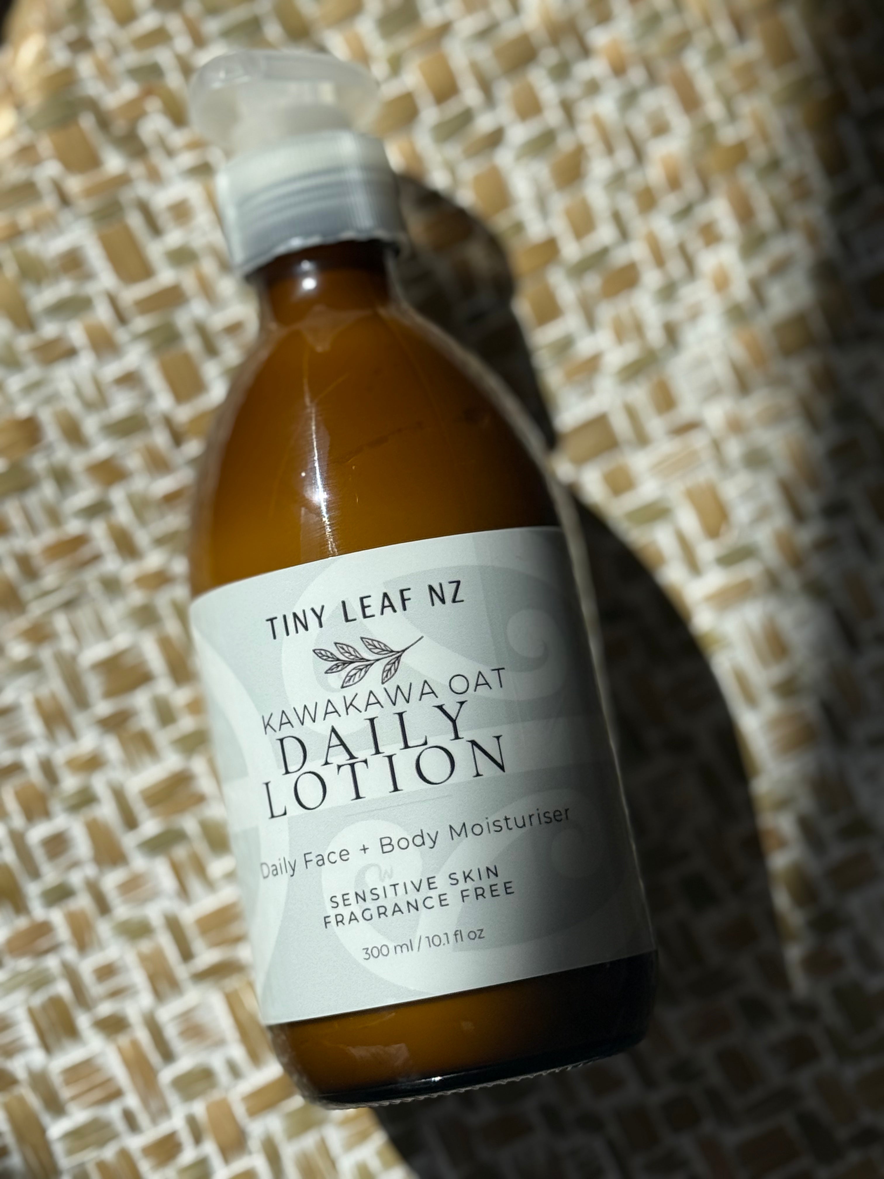 A bottle of Tiny Leaf Nz Kawakawa Oat Daily Lotion, 300 ml, featuring an amber brown bottle and a white label, resting on a woven straw surface.