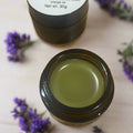 Small container of green substance on a wooden surface with a label above it.