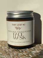 A jar of Tiny Leaf NZ Manuka Kawakawa Face Mask sits on a woven straw mat against a plain beige wall, casting a strong shadow to the right.