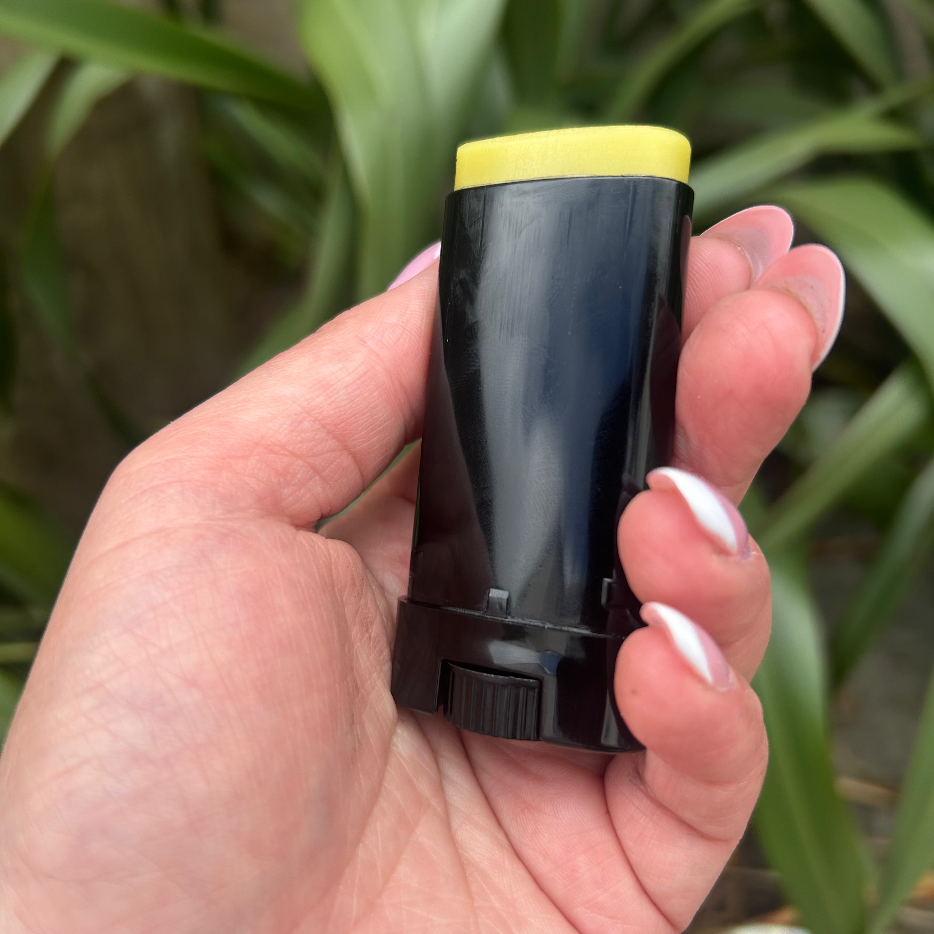 Hand holding a black and yellow cylindrical object with green foliage in the background