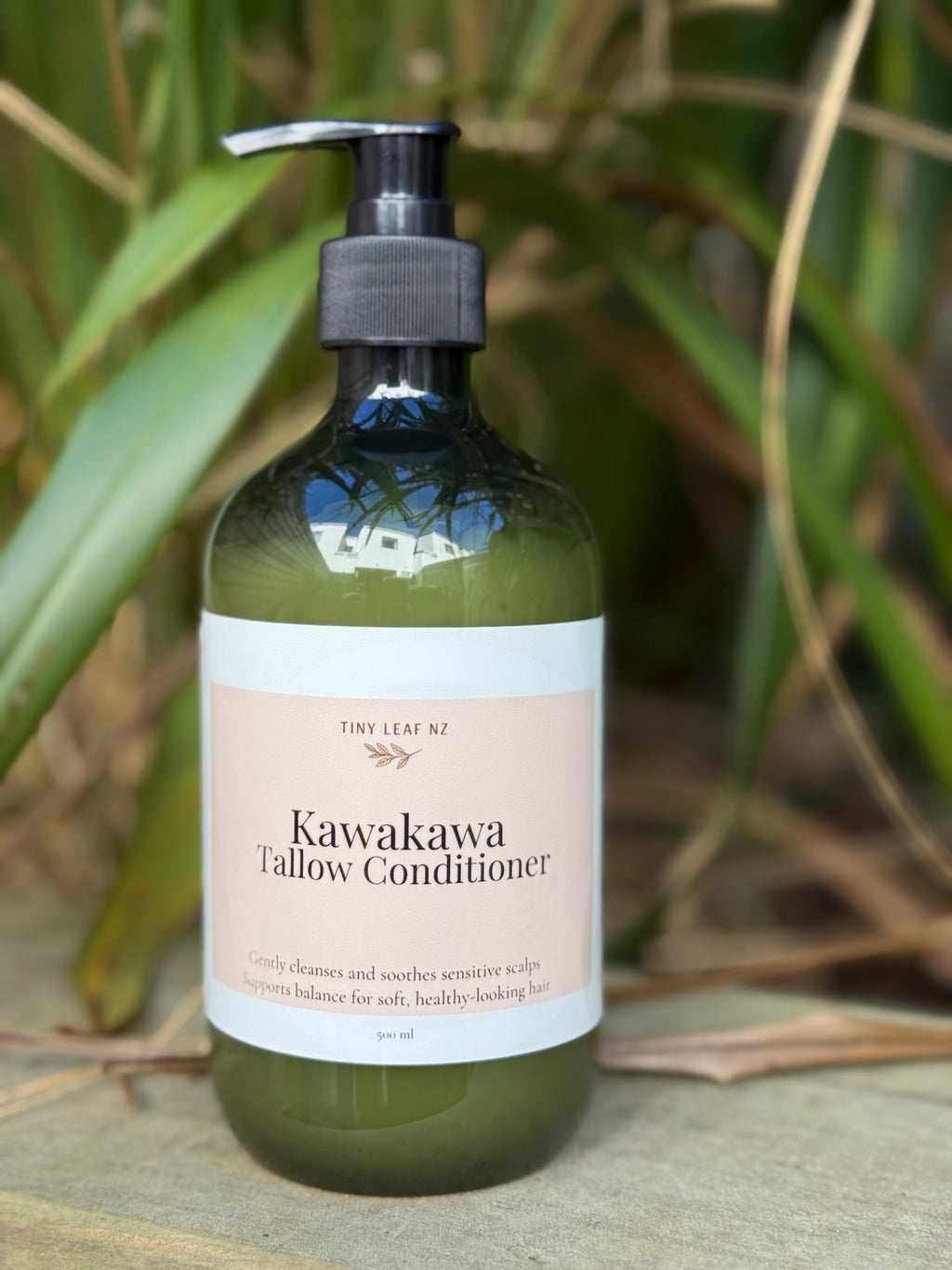 Green bottle of Kawakawa Tallow Conditioner with a pump on a natural background