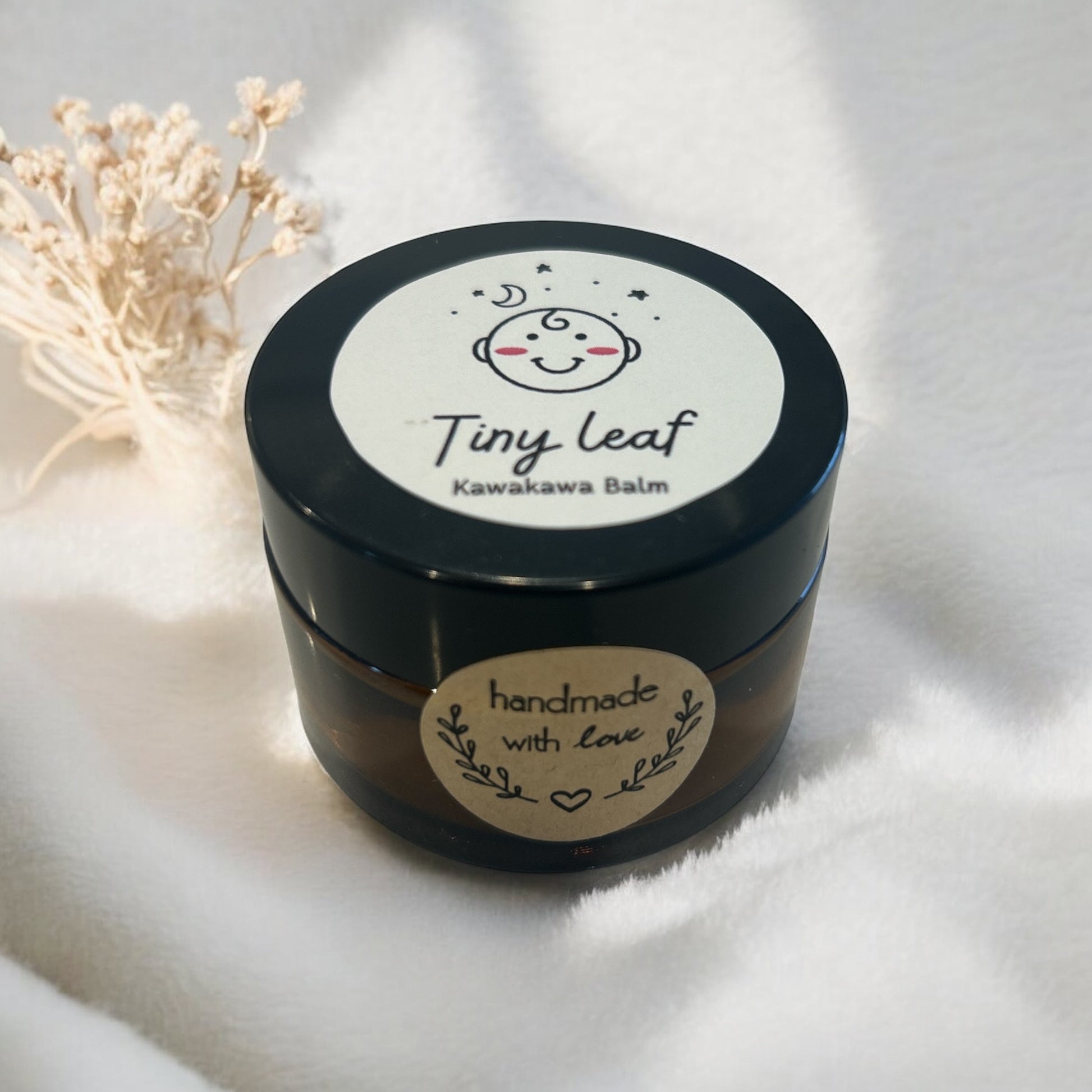 Black jar of kawakawa balm with 'Tiny Leaf' label on a white background