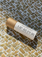 A lip balm stick labeled 'KAWAKAWA LIP REPAIR French Vanilla' resting diagonally on a woven straw mat under direct sunlight.