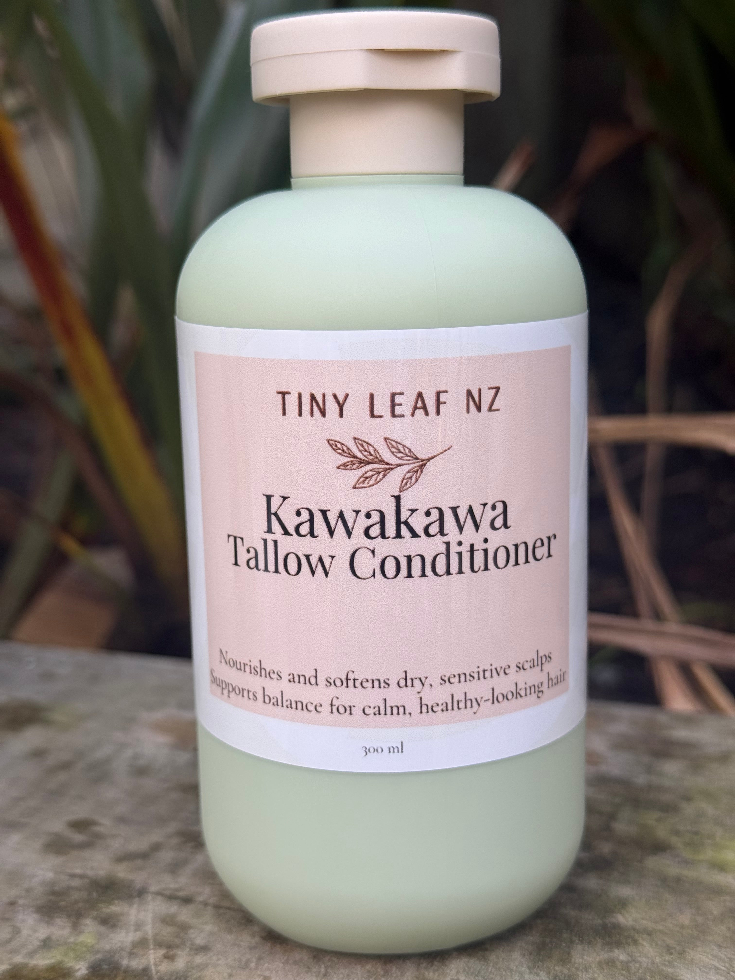 A bottle of Tiny Leaf NZ Kawakawa Tallow Conditioner lying diagonally on a textured stone surface with blurred natural foliage in the background.