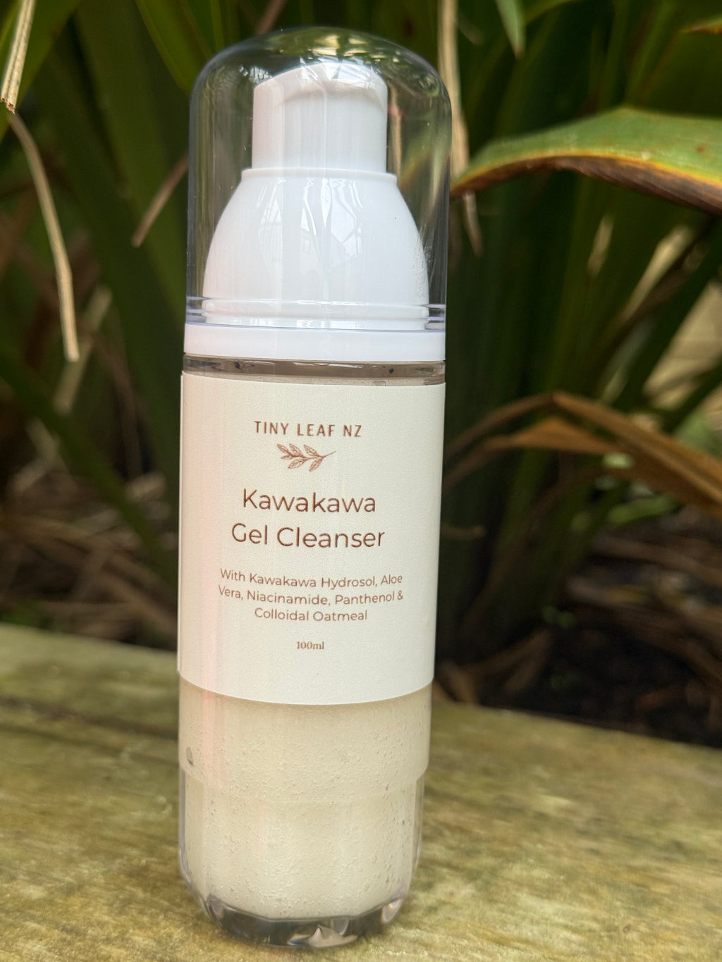 A 300ml bottle of Tiny Leaf NZ Kawakawa Gel Cleanser with a white pump and clear cap, set outdoors on a stone surface with green foliage in the background.