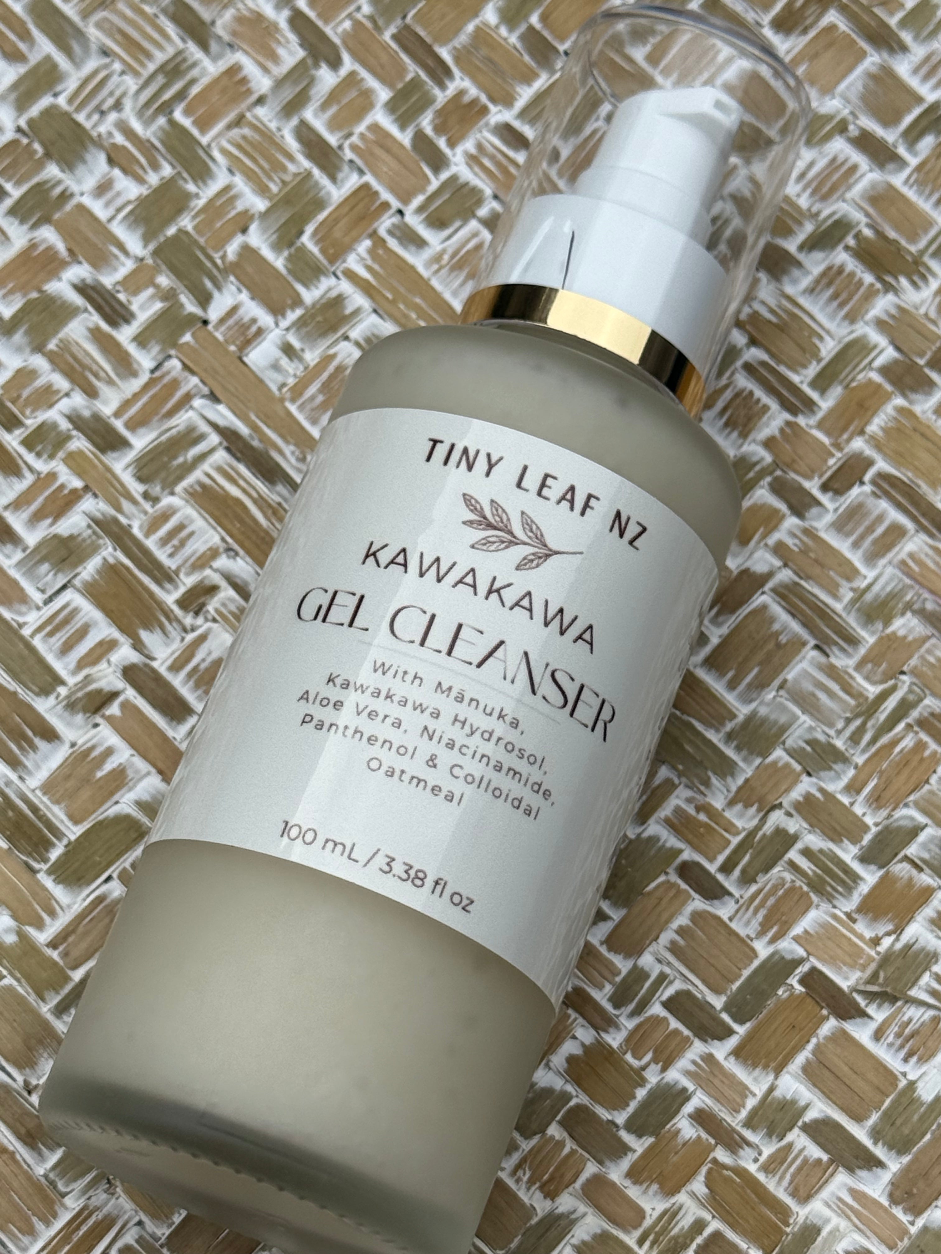 A bottle of Tiny Leaf Nz Kawakawa Gel Cleanser with a white pump and gold collar, resting on a woven straw mat background.