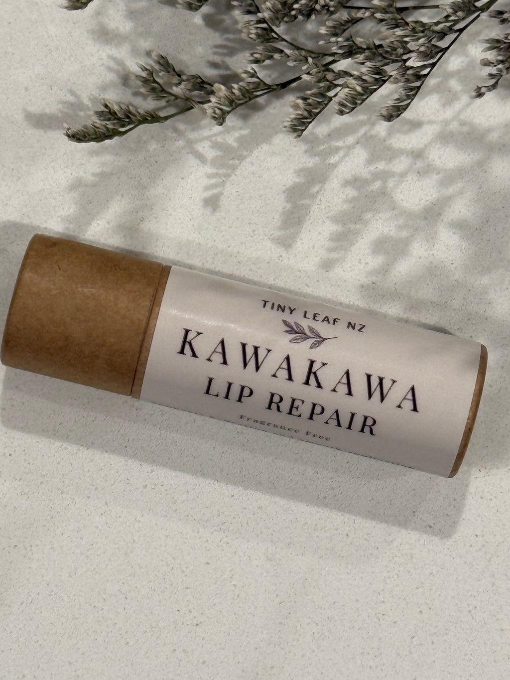 Kawakawa lip repair stick with brown paper wrap on a light surface