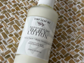 A bottle of Tiny Leak NZ Hawaiian Oat Body Lotion with a white pump dispenser, lying diagonally on a woven brown and beige textured mat.