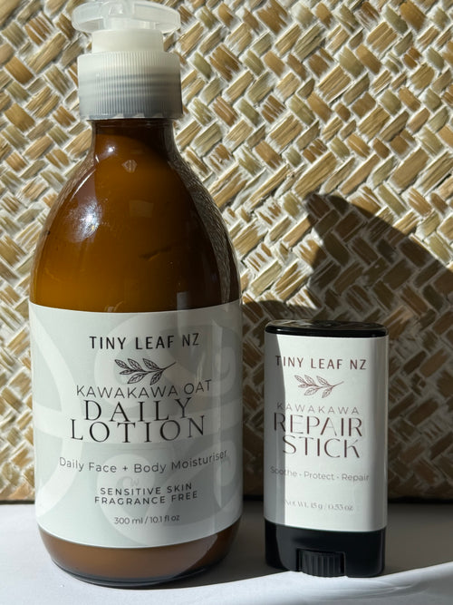 A bottle of Tiny Leaf NZ Kawakawa Oat Daily Lotion next to a matching stick of Tiny Leaf NZ Kawakawa Repair Stick, set against a woven straw background.