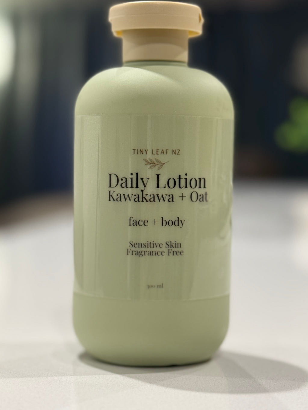 Minimalist product photo of Tiny Leaf NZ Daily Lotion Kawakawa + Oat in a soft sage green bottle on a white marble stone