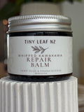 A jar of Tiny Leaf NZ Whipped Kawakawa Repair Balm with a white label and silver lid, displayed on a white ribbed pedestal.