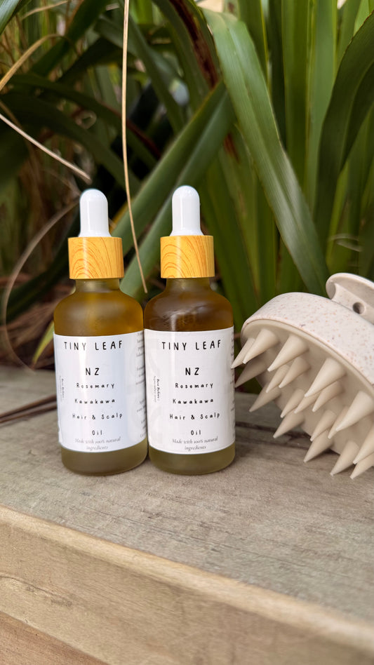 Two bottles of Tiny Leaf NZ hair and scalp oil with a hairbrush on a wooden surface.