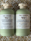 Two pale sage green bottles of Tiny Leaf Nz hair care products, labeled Kawakawa Tallow Shampoo and Kawakawa Tallow Conditioner, placed side by side on a woven beige and white mat.