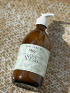 A bottle of Tiny Leaf NZ Kawakawa Tallow Body Wash with a white pump dispenser, resting on a textured woven mat.
