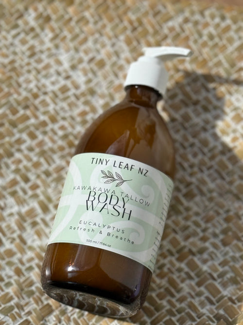 A bottle of Tiny Leaf NZ Kawakawa Tallow Body Wash with a white pump dispenser, resting on a textured woven mat.