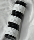 Three dark glass jars with white labels reading 'The Leaf NZ' and 'Jalopy Mauna Loa' arranged diagonally on a white fabric background.