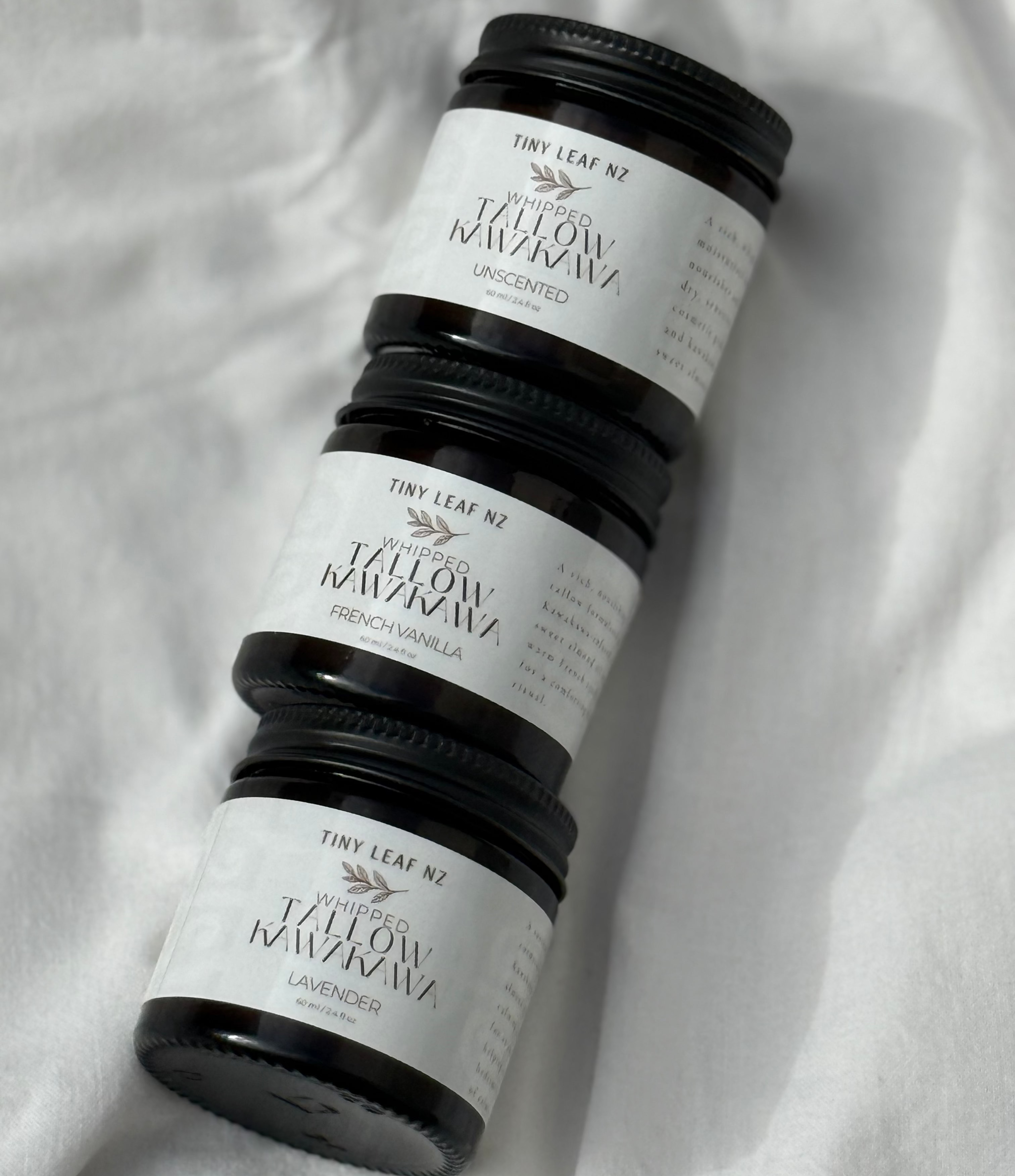 Three dark glass jars with white labels reading 'The Leaf NZ' and 'Jalopy Mauna Loa' arranged diagonally on a white fabric background.