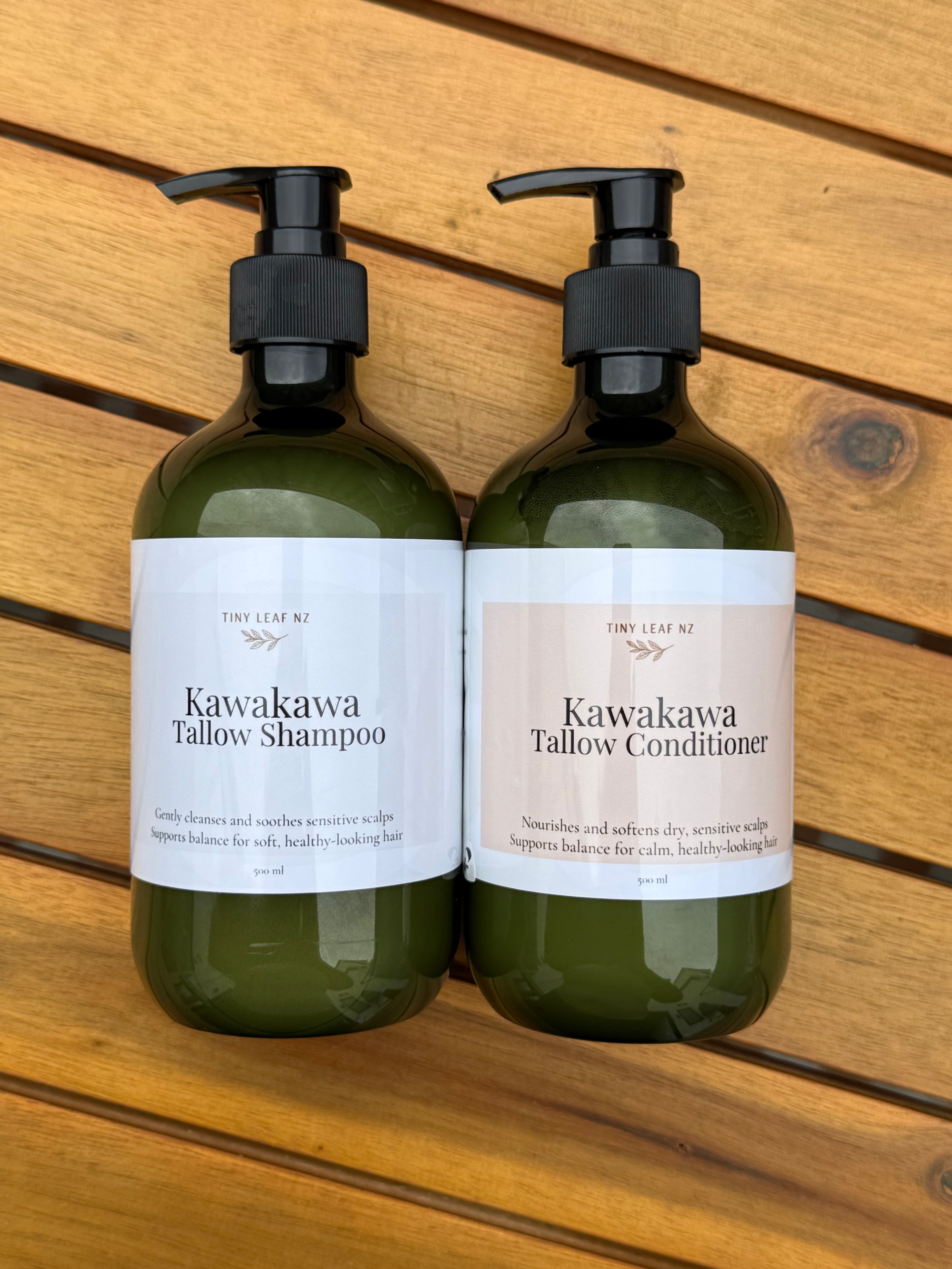 Two bottles of Kawakawa Tallow Shampoo and Conditioner on a wooden surface