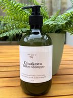 Bottle of Kawakawa Tallow Shampoo on a wooden surface with green plants in the background