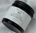 A small black jar of Tiny Leaf NZ Whipped Waxowhaukawa Unscented wax, shown on a textured white fabric background.