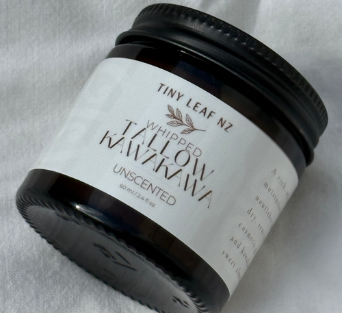 A small black jar of Tiny Leaf NZ Whipped Waxowhaukawa Unscented wax, shown on a textured white fabric background.