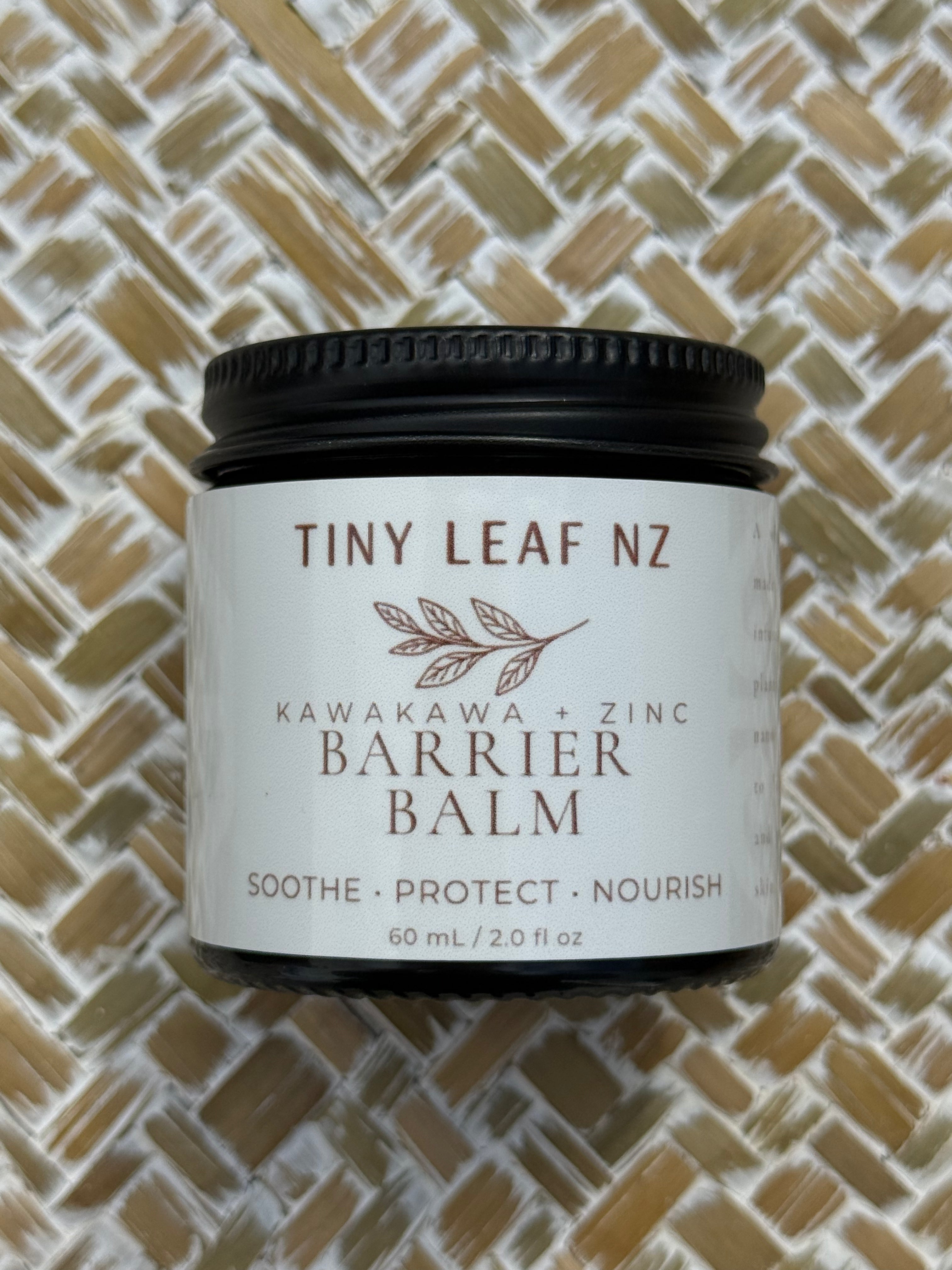 A jar of Tiny Leaf NZ Kawakawa + Zinc Barrier Balm with a black lid and white label, placed on a woven straw mat background.