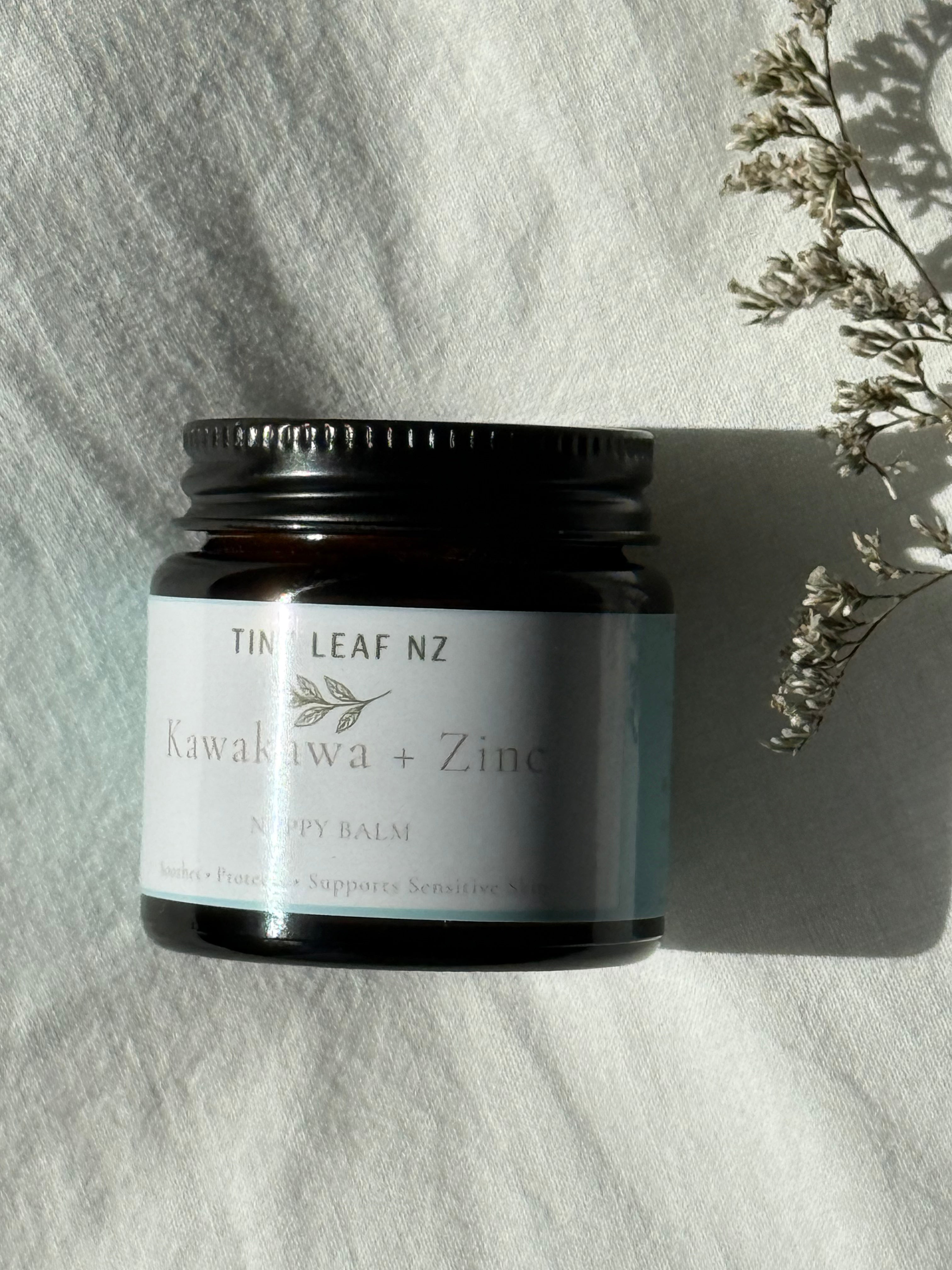 Jar of Tiny leaf NZ Kawakawa + Zinc balm on a textured surface with a branch in the corner.