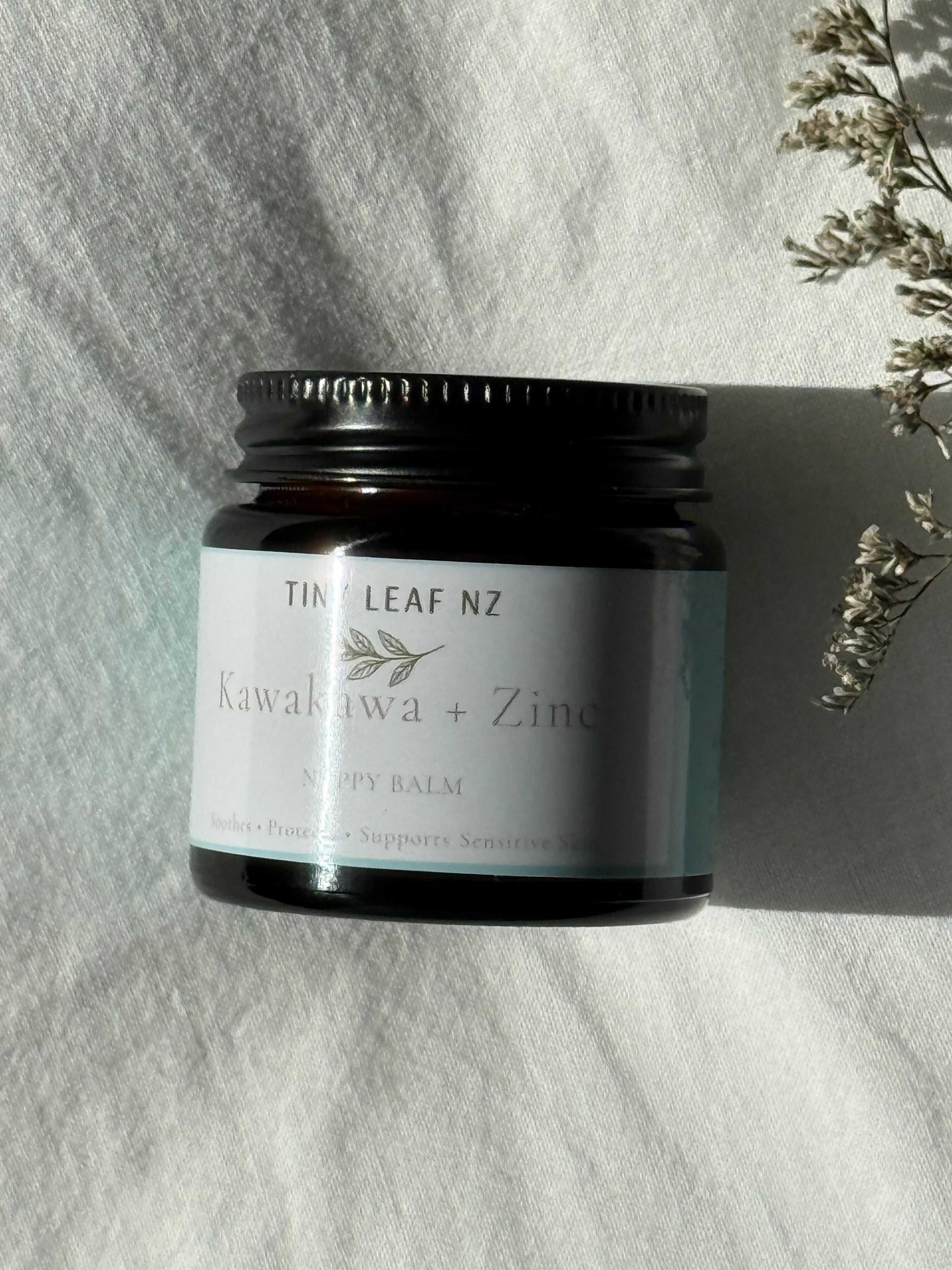 Tin of Tiny leaf NZ balm on a textured white surface with dried flowers.