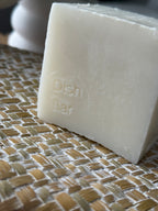 A close-up of a rectangular bar of off-white dish soap embossed with the words 'Dish Bar', resting on a woven beige and white placemat.