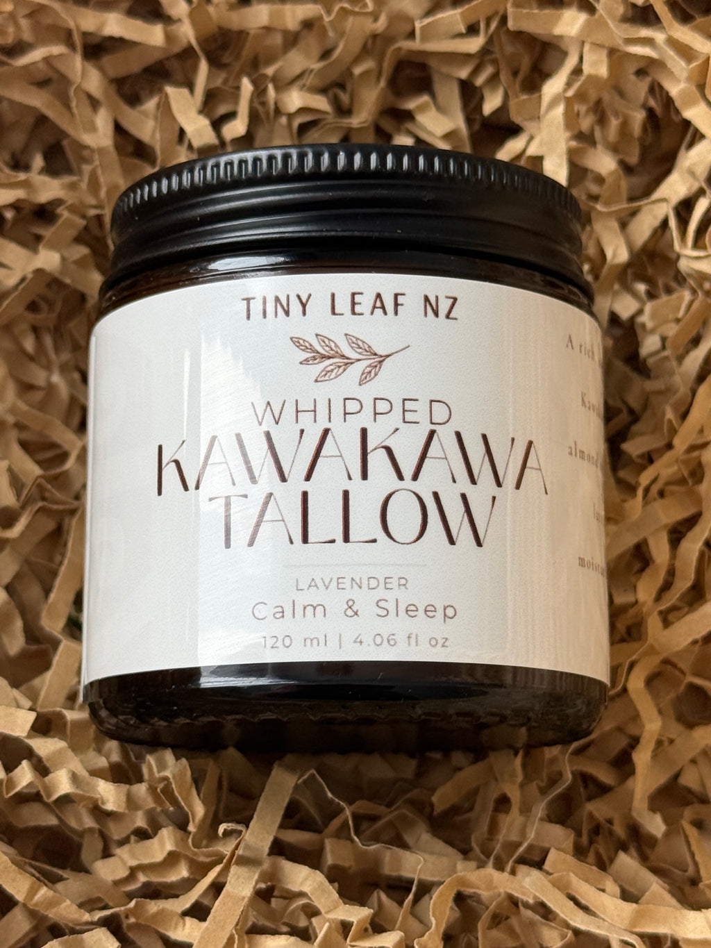 A jar of Tiny Leaf NZ Whipped Kawakawa Tallow body butter, labeled Lavender Calm & Sleep, resting on brown shredded paper packaging.