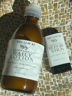 Tiny Leaf Nz Kawakawa Oat Daily Lotion in an amber glass bottle and Kawakawa Repair Stick in a black tube, both with white labels, displayed on a woven straw mat.