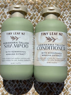 Two pale sage green bottles of Tiny Leaf NZ hair care products, labeled Kawakawa Tallow Shampoo and Kawakawa Tallow Conditioner, placed side by side on a woven mat background.