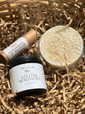Three natural skincare products arranged in brown shredded paper: a round beige soap bar wrapped in clear plastic, a small kraft tube labeled Kawakawa Lip Repair, and a black jar labeled Tiny Leaf Nz Whipped Yellow Wax Wax Unscented.