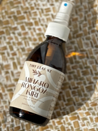 A bottle of Miharo Rongoa Kuri facial mist by Tiny Leaf NZ, featuring an amber glass bottle, white spray nozzle, and a beige label, resting on a woven brown and beige textured mat.