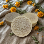 Three circular soap bars with floral designs on a textured fabric background with yellow flowers.