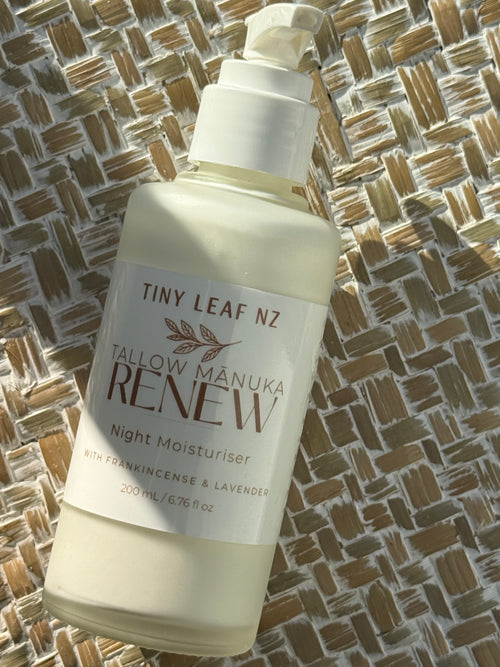 A bottle of Tiny Leaf NZ Tallow Manuka Renew Night Moisturiser, filled with a creamy off-white liquid, resting on a woven straw mat.