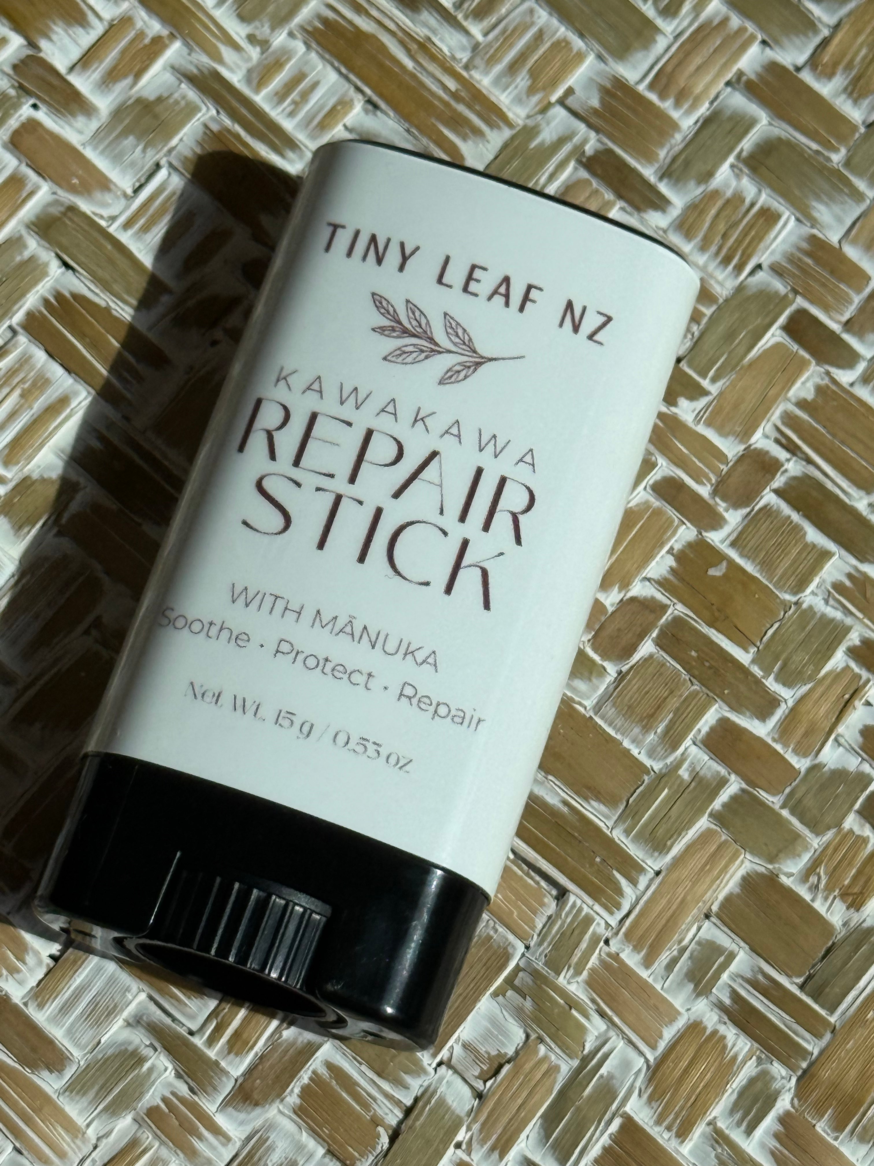 A cylindrical skincare stick container labeled 'Tiny Leaf Nz Kawakawa Repair Stick' with a white label and black cap, placed on a woven straw mat background.
