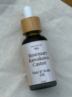 Bottle of Rosemary Kawakawa Castor Hair & Scalp Oil with a dropper on a textured fabric background