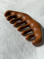 A wooden five-toe comb with a rich brown finish, resting on a textured light gray fabric background.