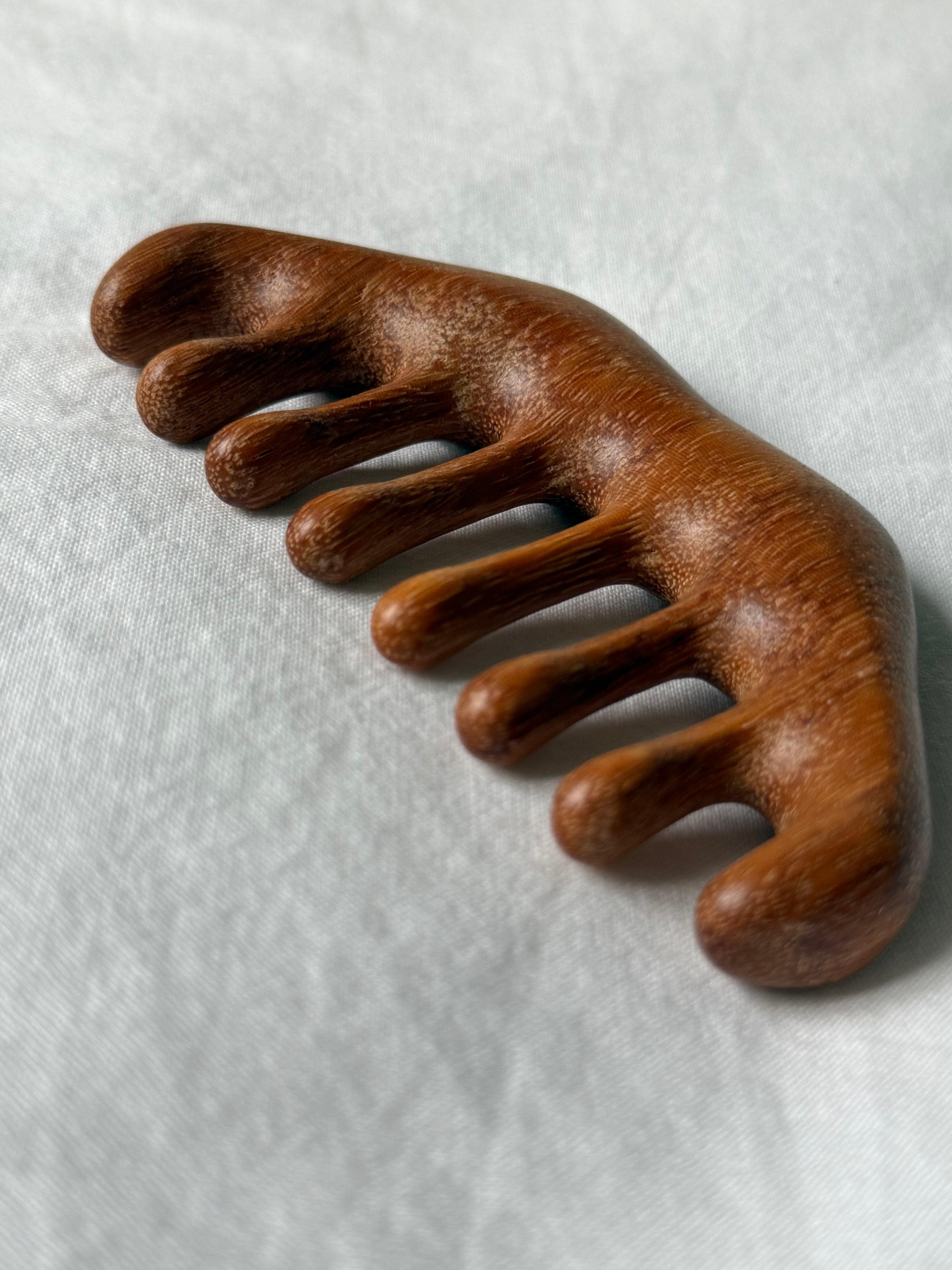 A wooden five-toe comb with a rich brown finish, resting on a textured light gray fabric background.